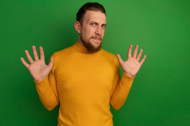 Free photo unpleased handsome blonde man stands with raised hands isolated