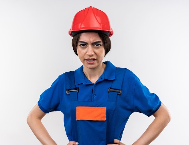 Free photo unpleased looking at camera young builder woman in uniform holding hands on hip