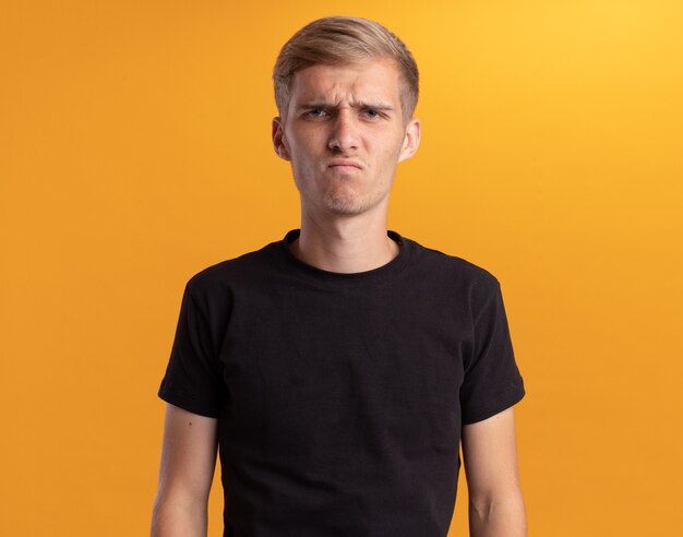 Unpleased looking at front young handsome guy wearing black shirt isolated on yellow wall