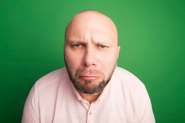 Free photo unpleased looking middle-aged bald man wearing pink t-shirt