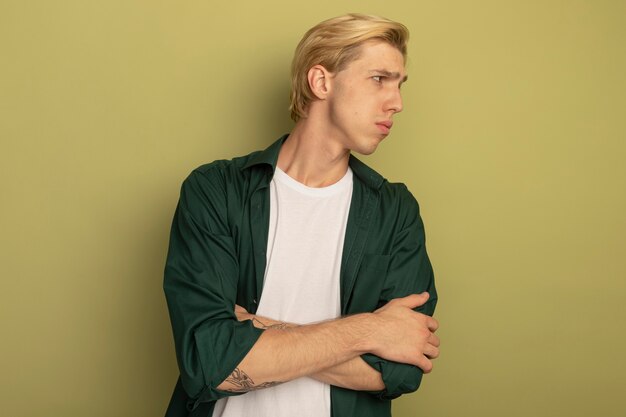 Unpleased looking at side young blonde guy wearing green t-shirt crossing hands