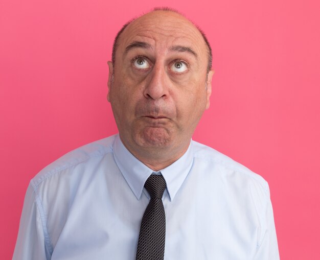 Unpleased looking up middle-aged man wearing white t-shirt with tie isolated on pink wall