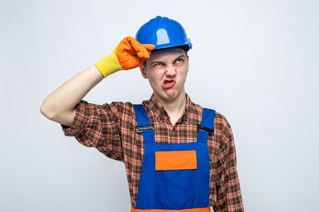 Unpleased looking up young male builder wearing uniform with gloves 
