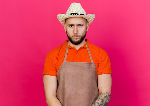 Unpleased male gardener wearing gardening hat looks at camera