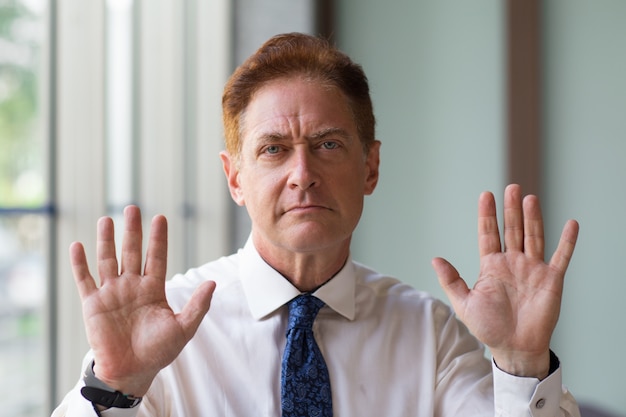 Unpleased mature businessman showing stop gesture