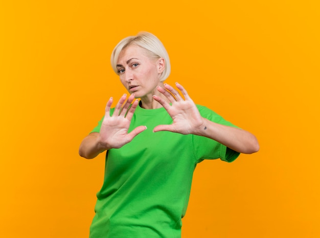 Unpleased middle-aged blonde slavic woman looking at camera doing no gesture isolated on yellow background
