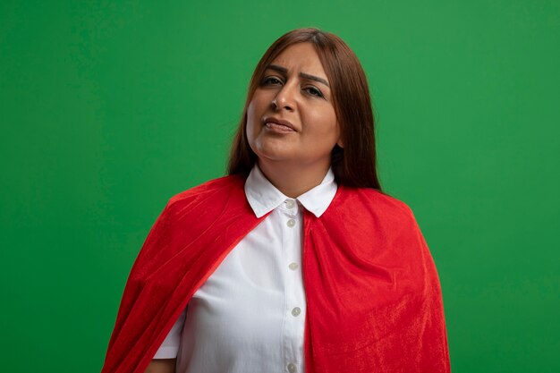 Unpleased middle-aged superhero female looking at camera isolated on green background