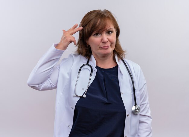 医療ローブと孤立した白い背景の上の頭の近くに手を置く聴診器を着て不快な中年女性医師