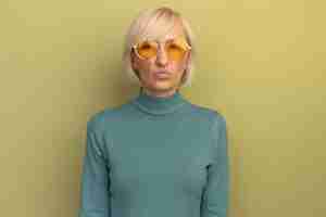 Free photo unpleased pretty blonde slavic woman in sun glasses looks at camera on olive green