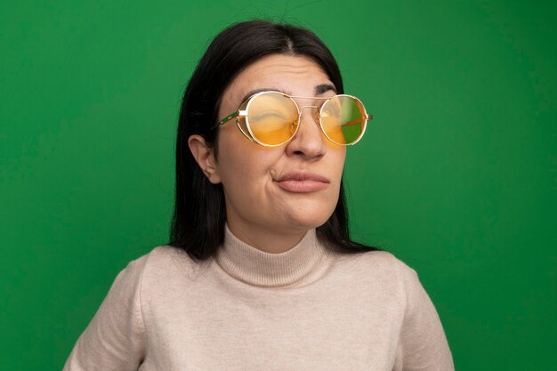 Недовольная красивая брюнетка кавказская девушка в солнцезащитных очках смотрит на зеленый