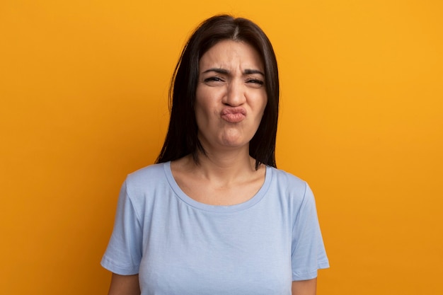 Unpleased pretty brunette woman looks at front isolated on orange wall