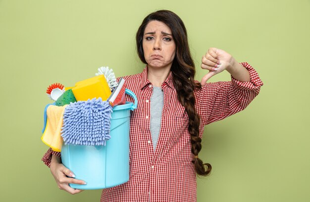 Unpleased pretty caucasian cleaner woman holding cleaning equipment and thumbing down looking at front