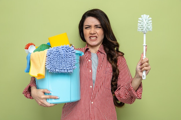 Unpleased pretty caucasian cleaner woman holding cleaning equipment and toilet brush 