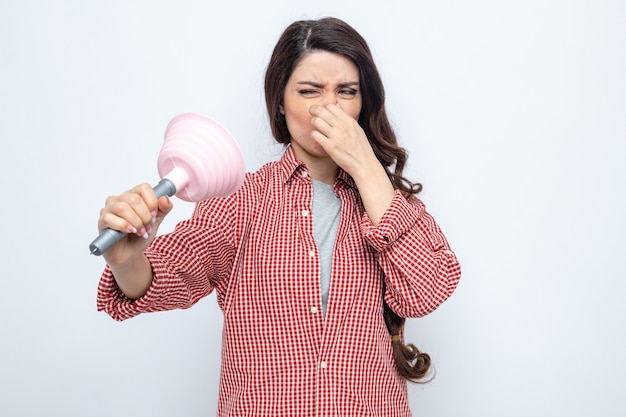 Unpleased pretty caucasian cleaner woman holding rubber plunger and closing her nose
