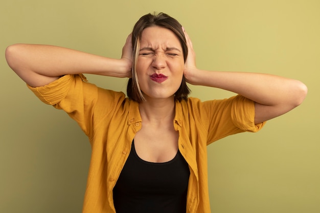 Free photo unpleased pretty caucasian woman closes ears with hands on olive green