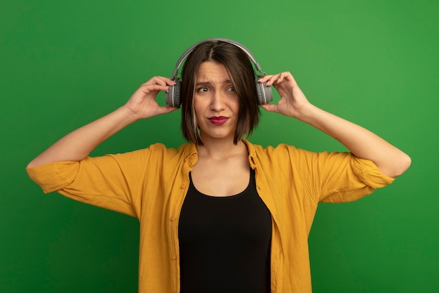 Free photo unpleased pretty caucasian woman on headphones looking at side on green