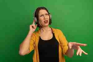 Free photo unpleased pretty caucasian woman on headphones looks and points at side on green