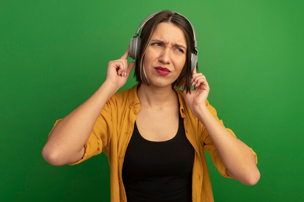 Unpleased pretty caucasian woman on headphones looks at side on green