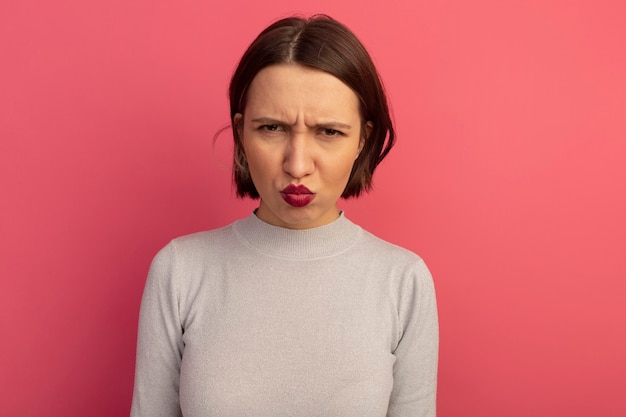 La donna abbastanza caucasica dispiaciuta esamina la macchina fotografica sul colore rosa