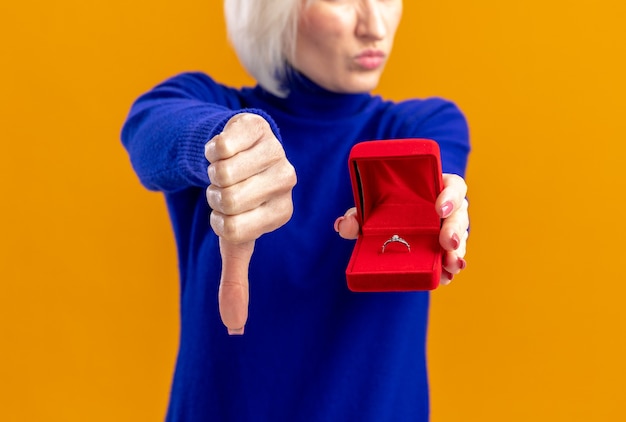 Free photo unpleased pretty slavic woman holding red ring box and thumbing down on valentine's day