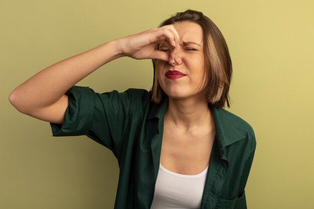 Unpleased pretty woman closes nose isolated on olive green wall