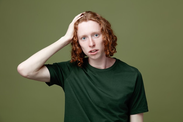 Unpleased putting hand on head young handsome guy wearing green t shirt isolated on green background