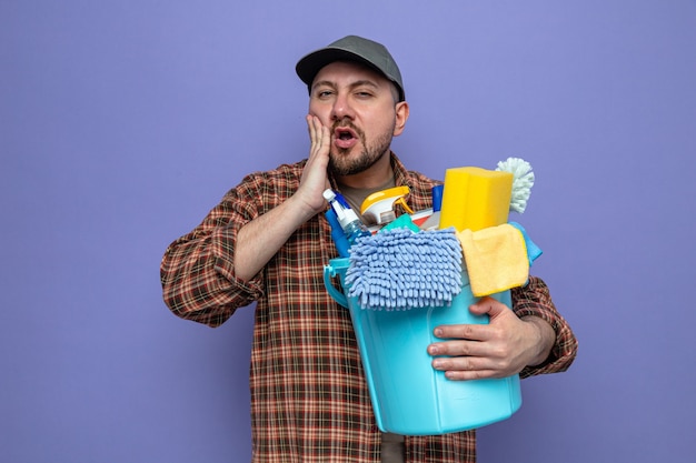 Unpleased slavic cleaner man holding cleaning equipment and 