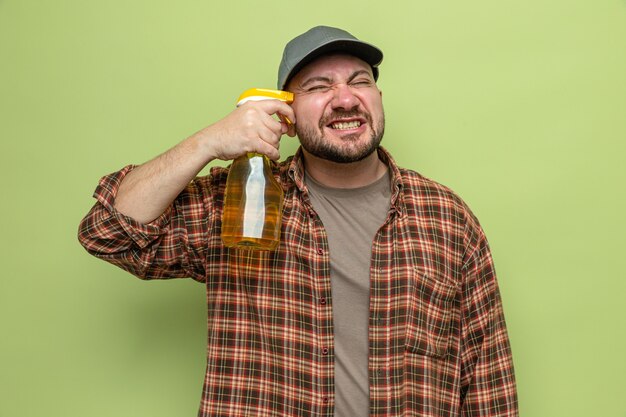 Unpleased slavic cleaner man holding spray cleaner to his tempe 