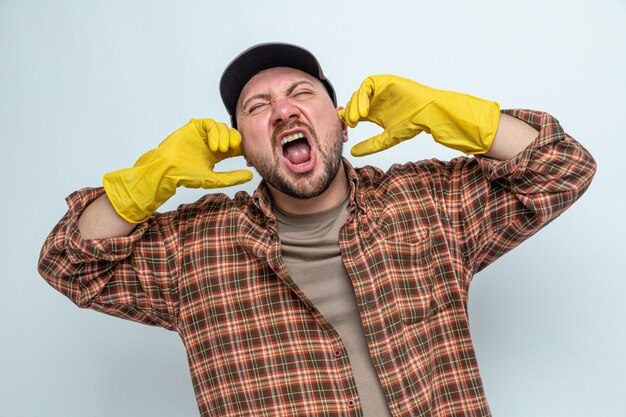 Unpleased slavic cleaner man with rubber gloves closing his ears with fingers