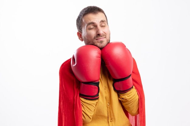 Foto gratuita l'uomo del supereroe dispiaciuto tiene i guantoni da boxe sotto il mento isolato sul muro bianco