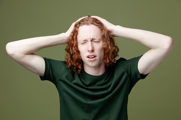 Unpleased with closed eyes grabbed head young handsome guy wearing green t shirt isolated on green background