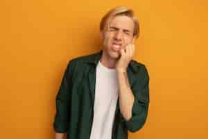 Free photo unpleased with closed eyes young blonde guy wearing green t-shirt putting hand on cheek