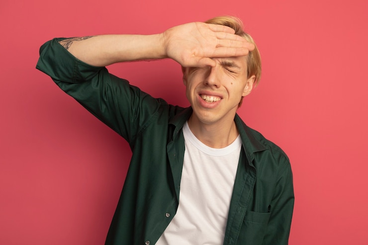 Free Photo unpleased with closed eyes young blonde guy wearing green t-shirt putting hand on forehead isolated on pink
