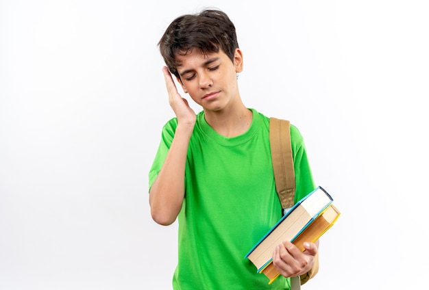 Unpleased with closed eyes young school boy wearing backpack holding books 