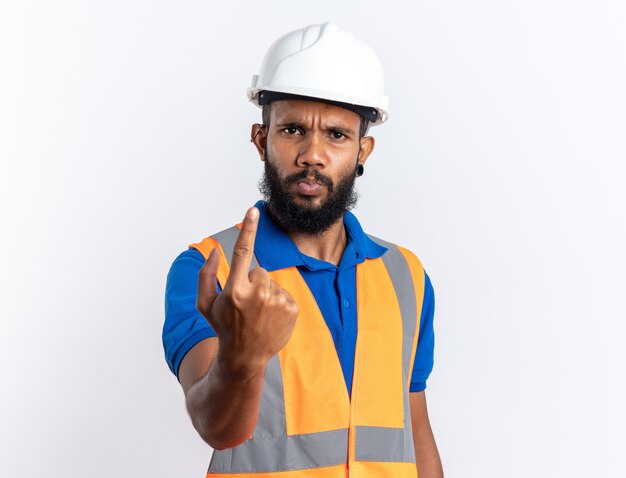 Unpleased young afro-american builder man in uniform with safety helmet pointing up isolated on white wall with copy space