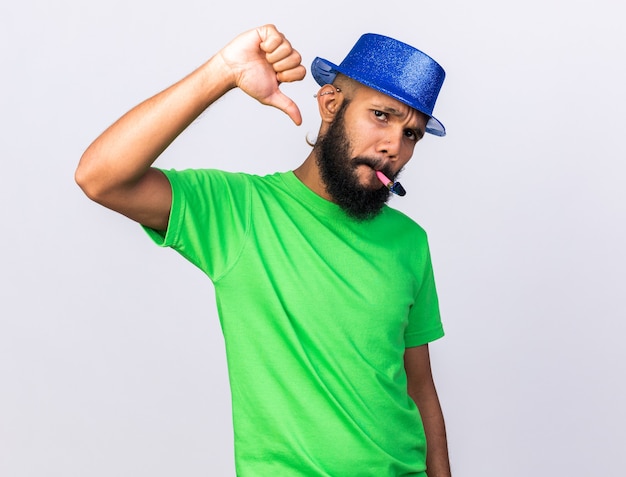 Недовольный молодой афро-американский парень в шляпе для вечеринки дует в свисток, показывая большой палец вниз