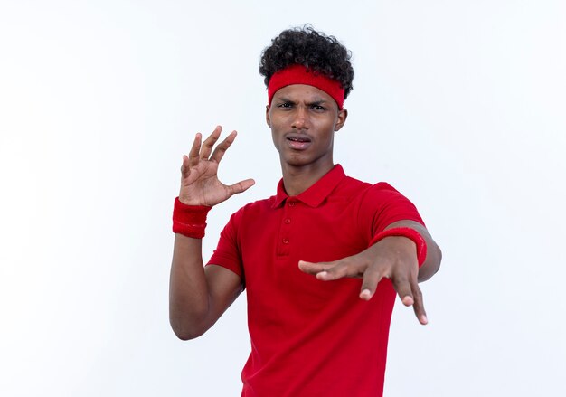 unpleased young afro-american sporty man wearing headband and wristband holding out hand at camera