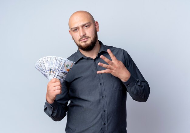 Unpleased young bald call center man holding money and showing four isolated on white background