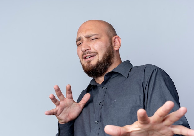 Unpleased young bald call center man stretching out hand gesturing no at camera isolated on white background