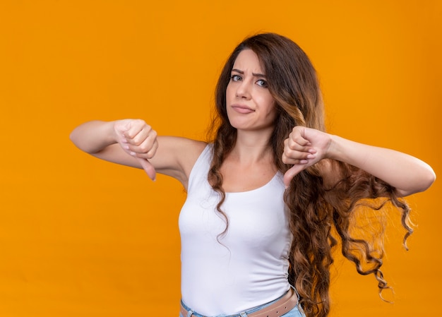 Foto gratuita giovane bella ragazza dispiaciuta che mostra i pollici giù sulla parete arancione isolata