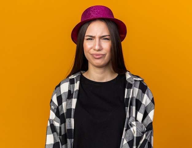 Una giovane bella ragazza scontenta che indossa un cappello da festa isolato sul muro arancione