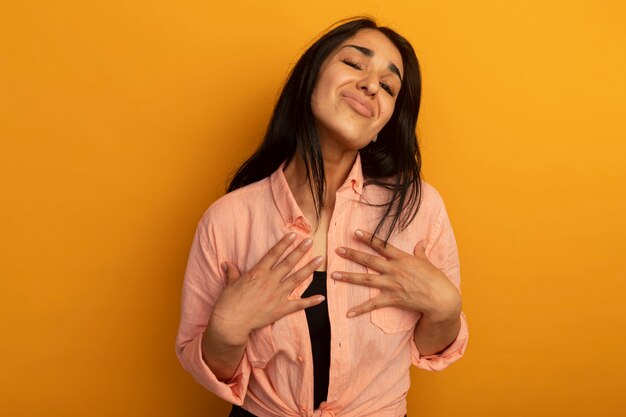 Unpleased young beautiful girl wearing pink t-shirt putting hands on herself isolated on yellow