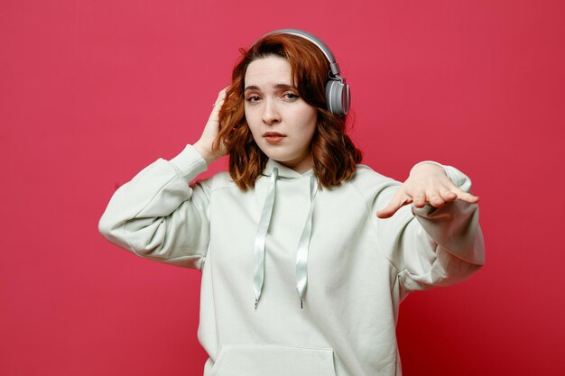Unpleased young beautiful girl in white sweater wearing headphones isolated on pink background