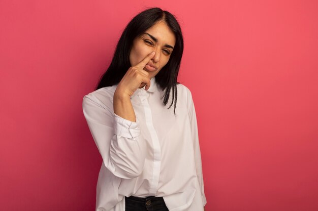 Unpleased young beautiful woman wearing white t-shirt putting finger on nose