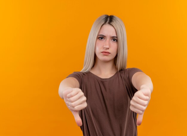 Unpleased young blonde girl showing thumbs down on isolated orange wall with copy space