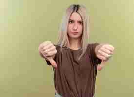 Бесплатное фото Недовольная молодая блондинка показывает палец вниз на изолированной зеленой стене с копией пространства