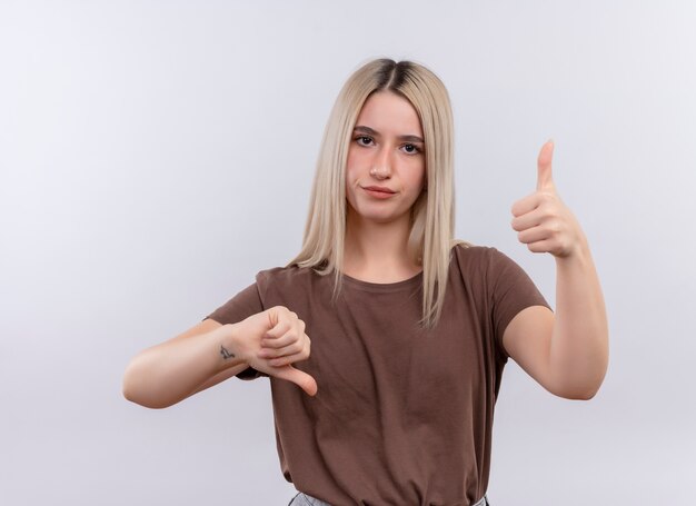 Unpleased young blonde girl showing thumbs up and down on isolated white wall