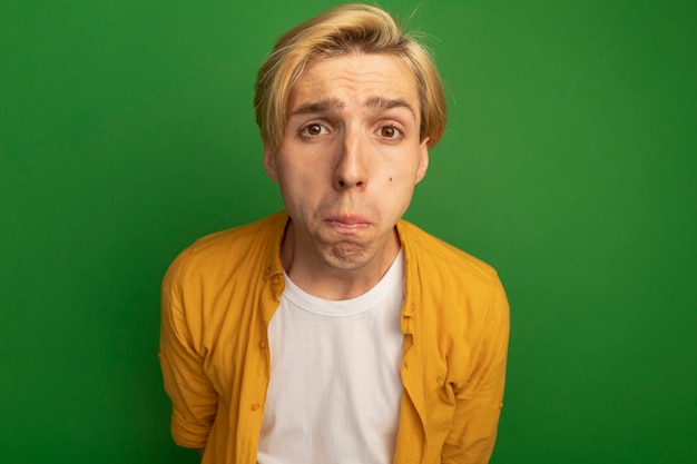 Free photo unpleased young blonde guy looking straight ahead wearing yellow t-shirt isolated on green