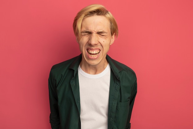 Free photo unpleased young blonde guy wearing green t-shirt holding hands on waist