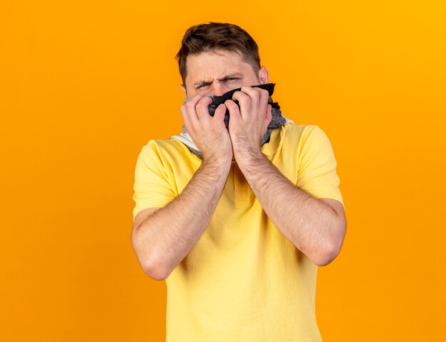 Unpleased young blonde ill slavic man wearing and holding scarf isolated on orange wall with copy space